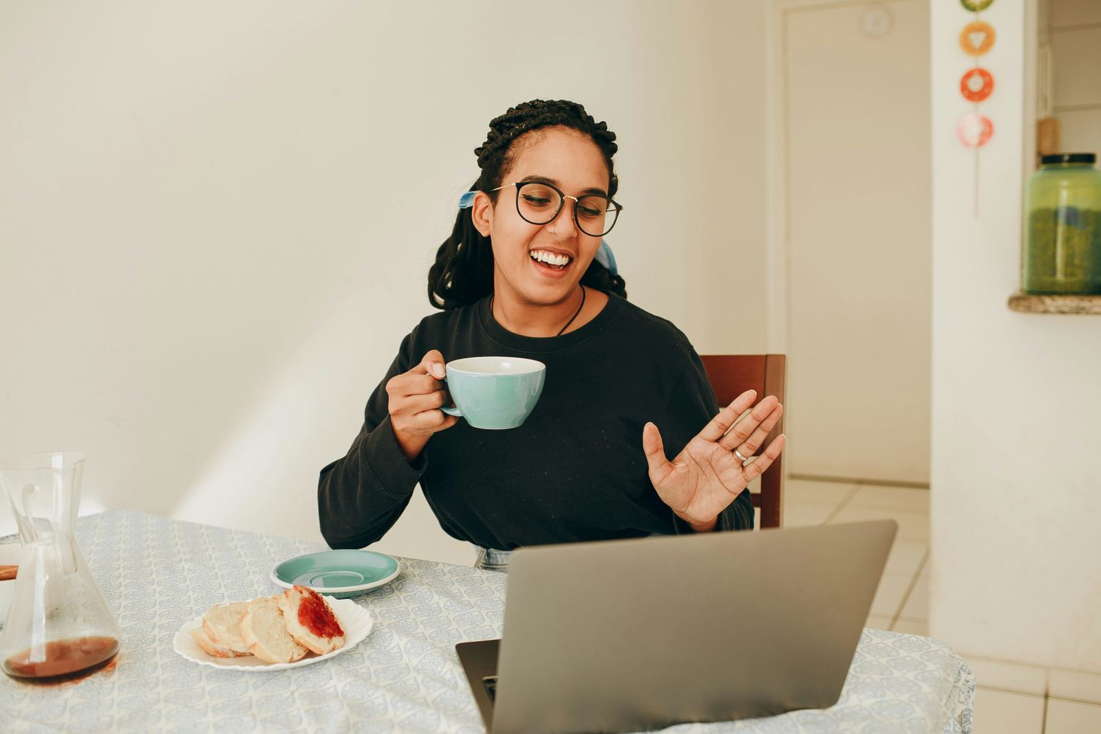 An image of a woman waving at someone on her webcam on laptop