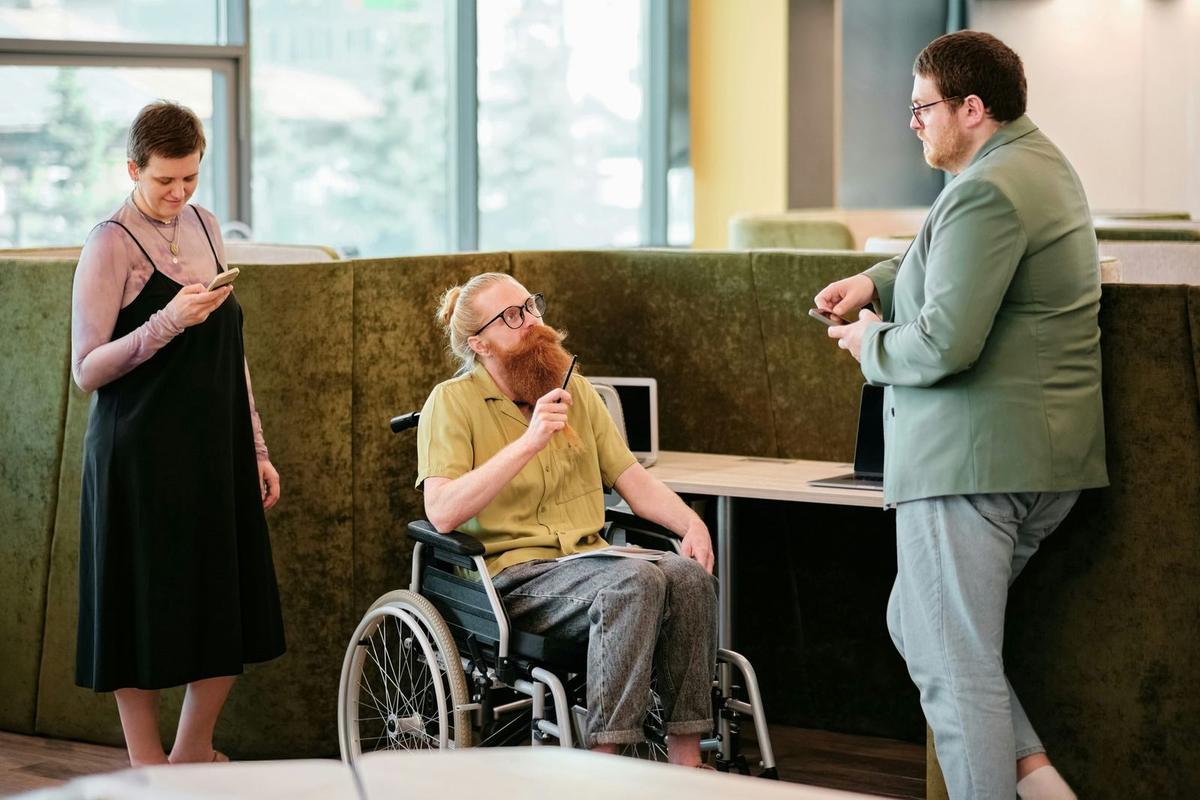 3 people in an office environment, 1 lady, 2 men and one of them in a wheelchair