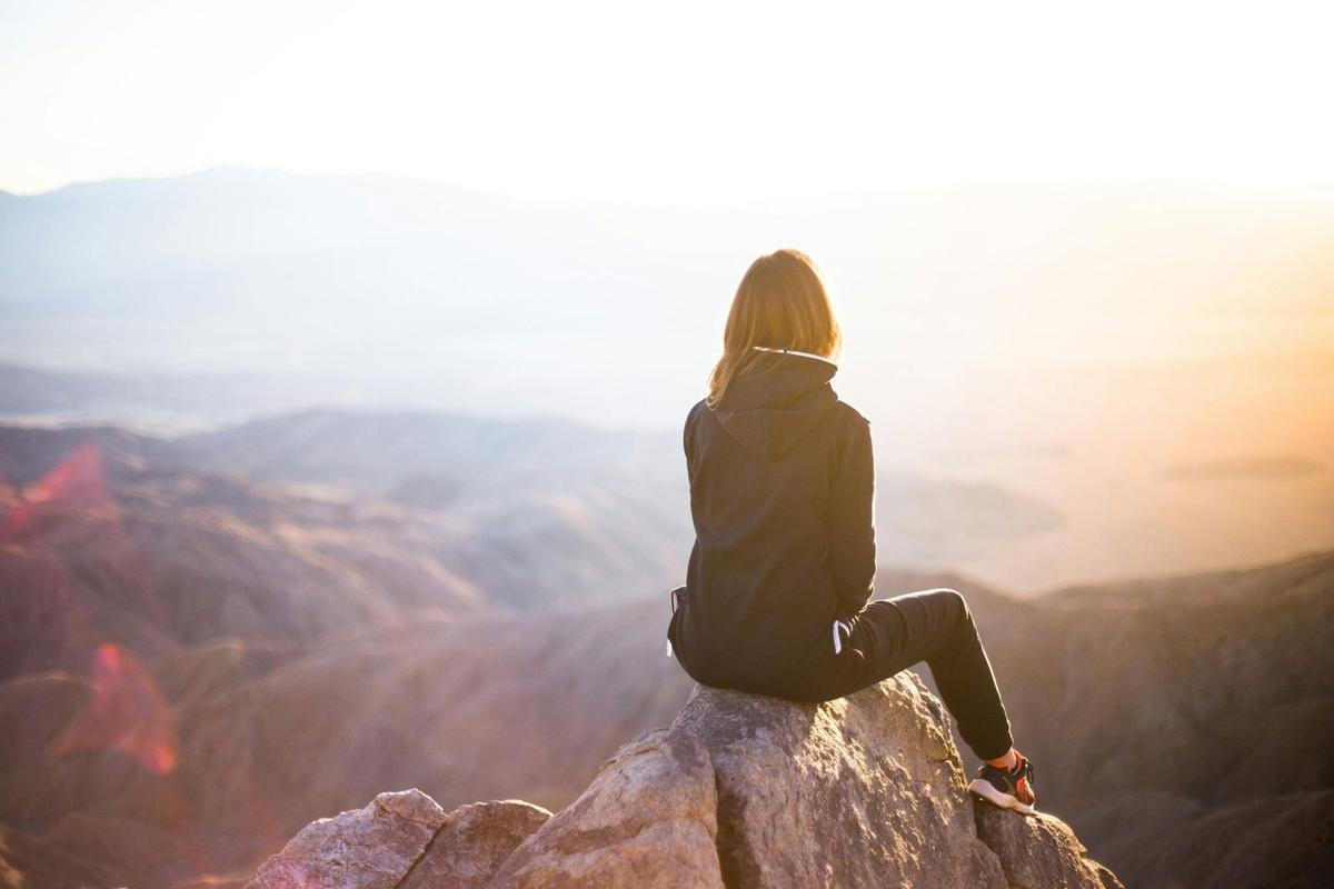 picture of a lady sat on top of a high up rock admiring the view below her