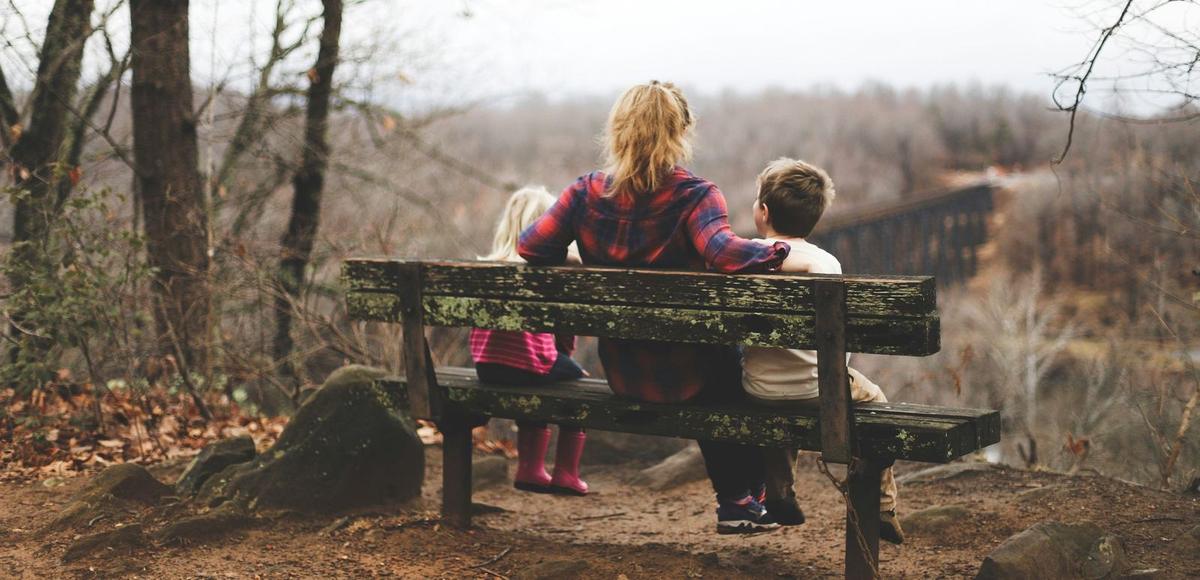 An image of a woman sat on bench with her children look at the view feeling free from domestic life