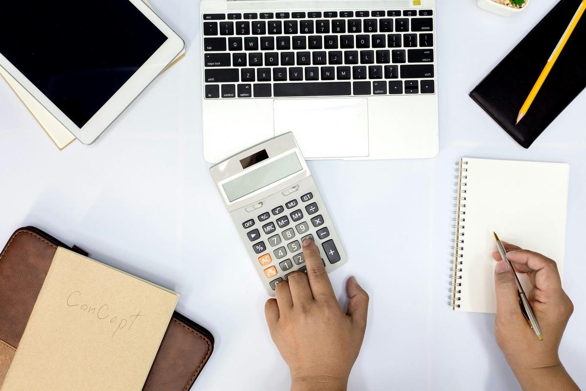 An image of hand using a calculator with books and laptop for billing