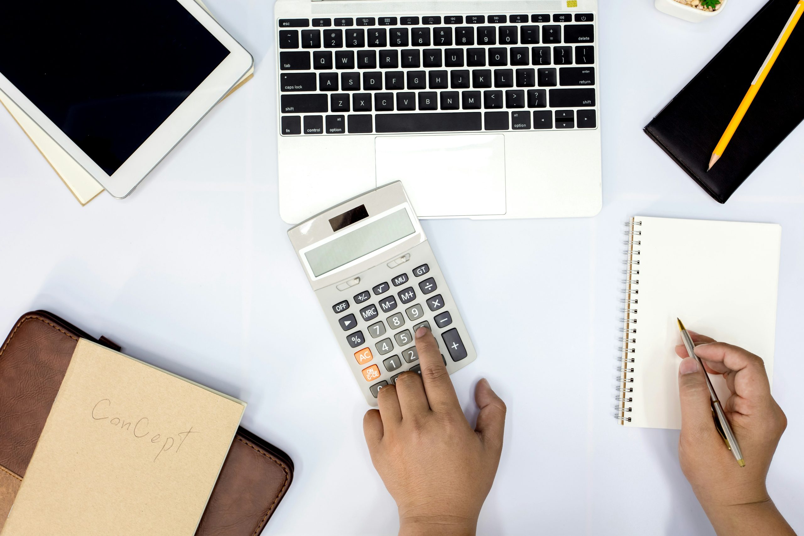 An image of hand using a calculator with books and laptop for billing